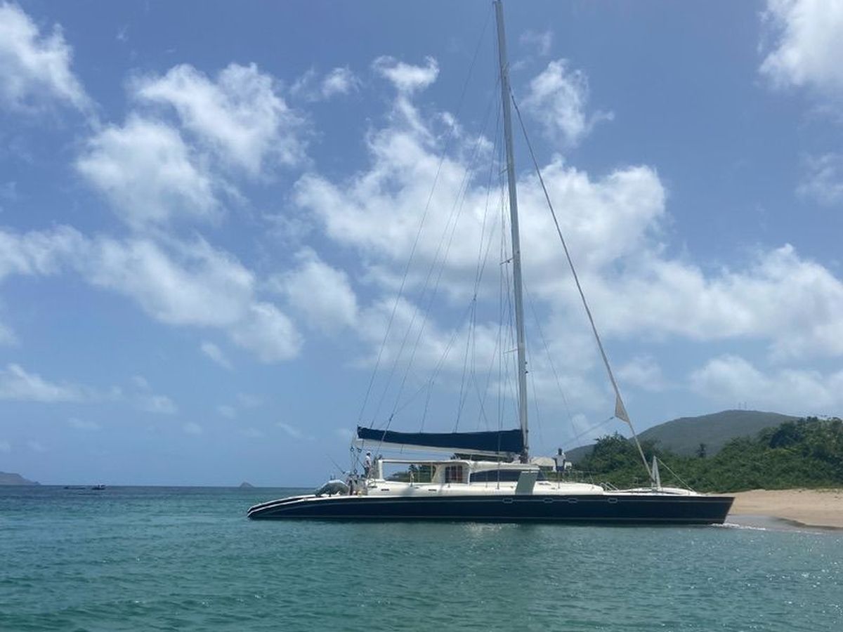 A catamaran anchored off a green headland